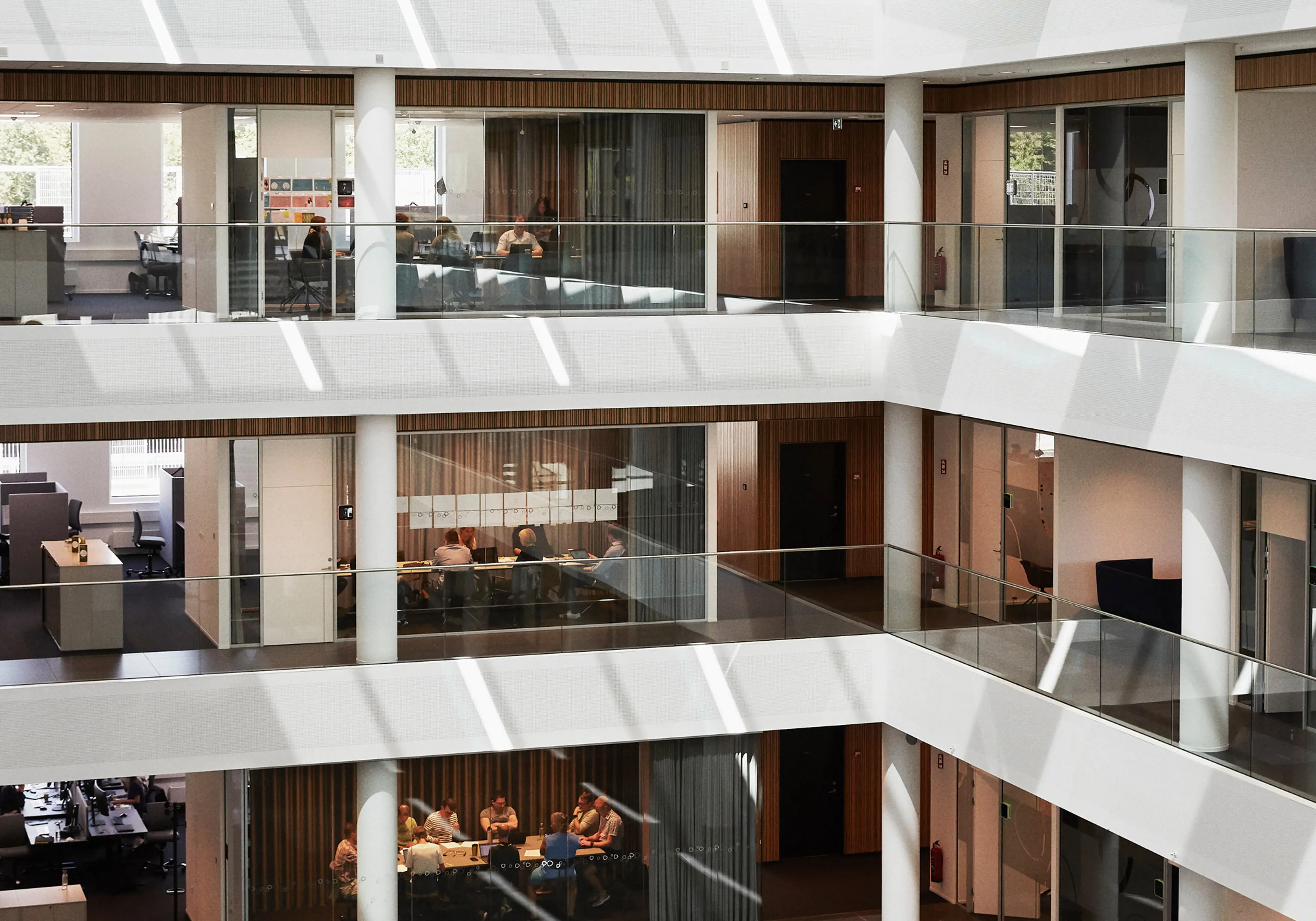 View of offices & meeting rooms spread over 3 levels: people are visible through transparent glass panels
